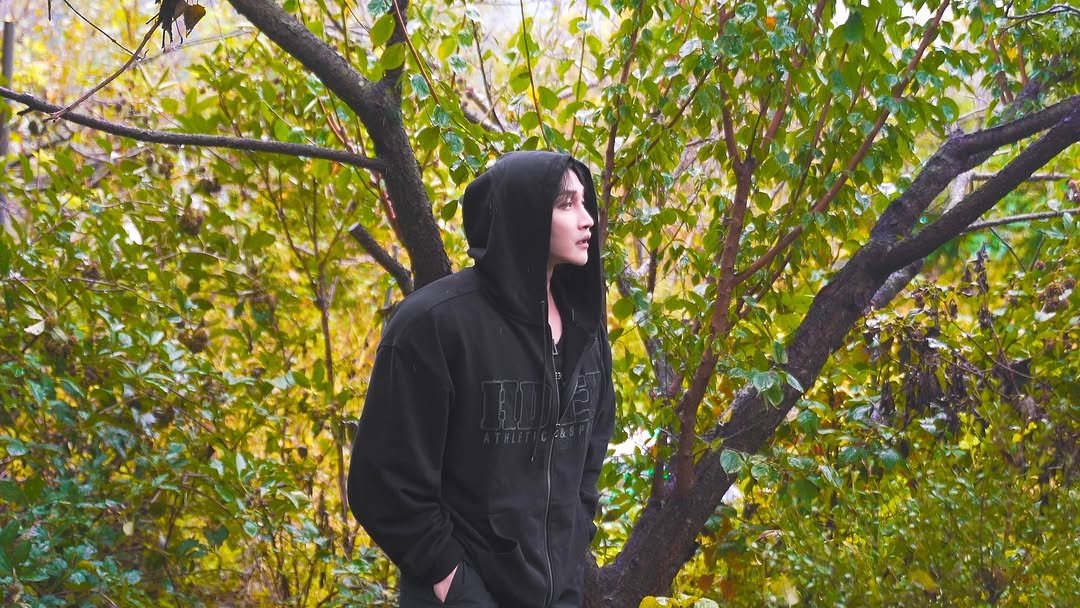 Photo shared by 조준 (Jun Cho) on October 26, 2025 tagging @hdex__official. May be an image of parka, cloak, tree, park and text.