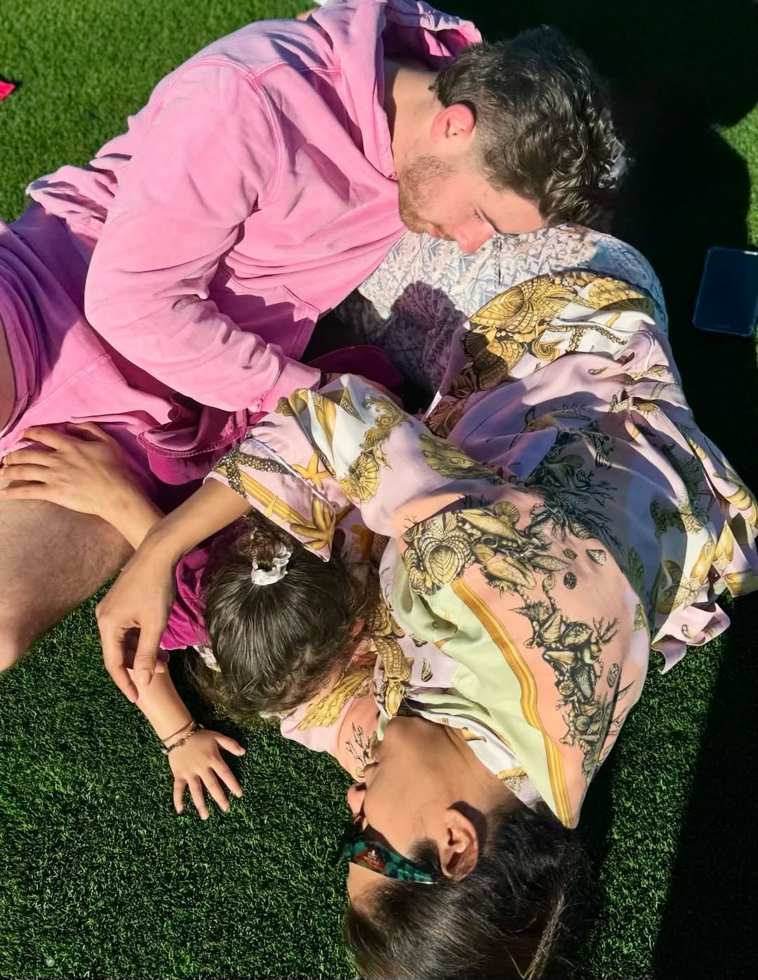 Photo shared by Priyanka on November 29, 2025 tagging @nickjonas, and @maltimarie. May be an image of child, people kissing, sleeping, grass, picnic and text.