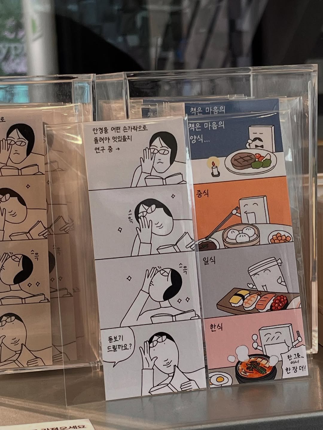 Photo shared by 큐새의 일일 | 인스타툰 on June 21, 2025 tagging @atypical.gallery. May be pop art of matchbook, newsstand and text that says '안정을어면손가락으로 안경을 어떤 손가락으로 올러아 올러아엇있을지 멋있을지 연구 연구중+ 중 책은 책은마음의 마음의 q 책은마음의 마음의 ម្រូយ is: 중식 ١1۱۱ α 일식 ٣۸ 돋보기 드릴까요? 한식 ร๊ิ 한그릇~ 아니 한장더! 더! 안 1152'.