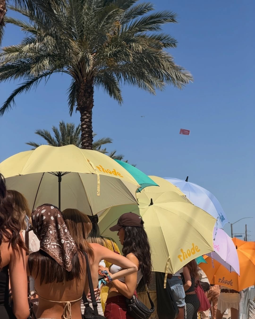 Photo shared by rhode skin on April 19, 2026 tagging @lilgalvin. May be an image of parasol, umbrella, crowd, palm trees and text.