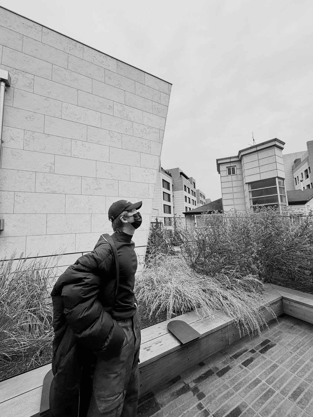 Photo by RM on January 27, 2026. May be a black-and-white image of standing, duffle coat, overcoat, parka, street, buildings and text.