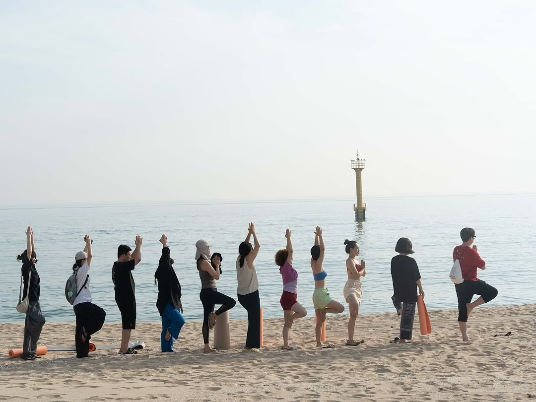 Photo shared by 요가 고우 on August 06, 2025 tagging @shinhyeaa. May be an image of 11 people, people practicing yoga, people standing, beach and text.
