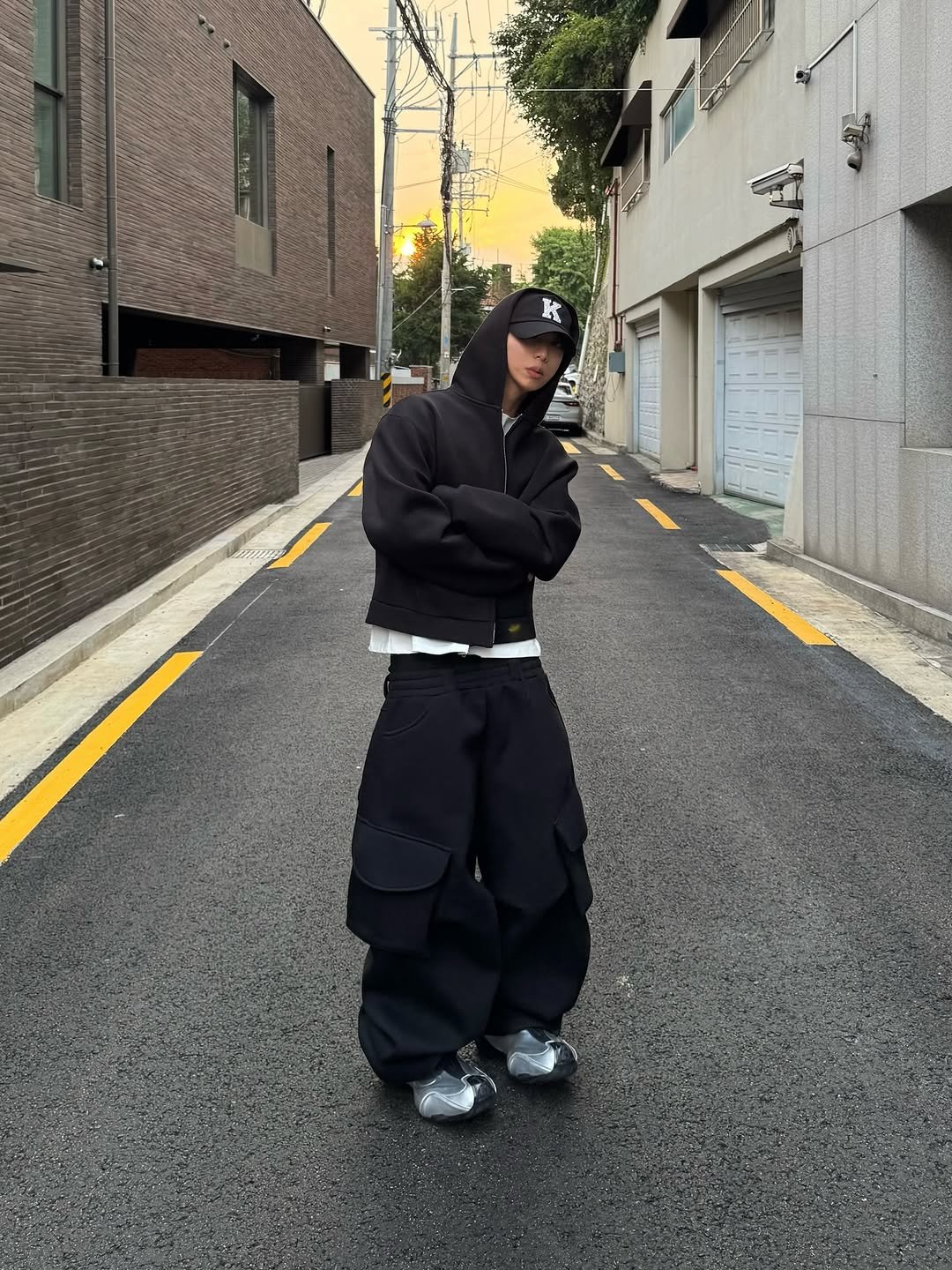 Photo shared by 소코년 sokonyun on October 04, 2025 tagging @mjd_official, and @koinseoul. May be an image of 1 person, face mask, cloak, sweatpants, parka, sweatsuit, street and text.