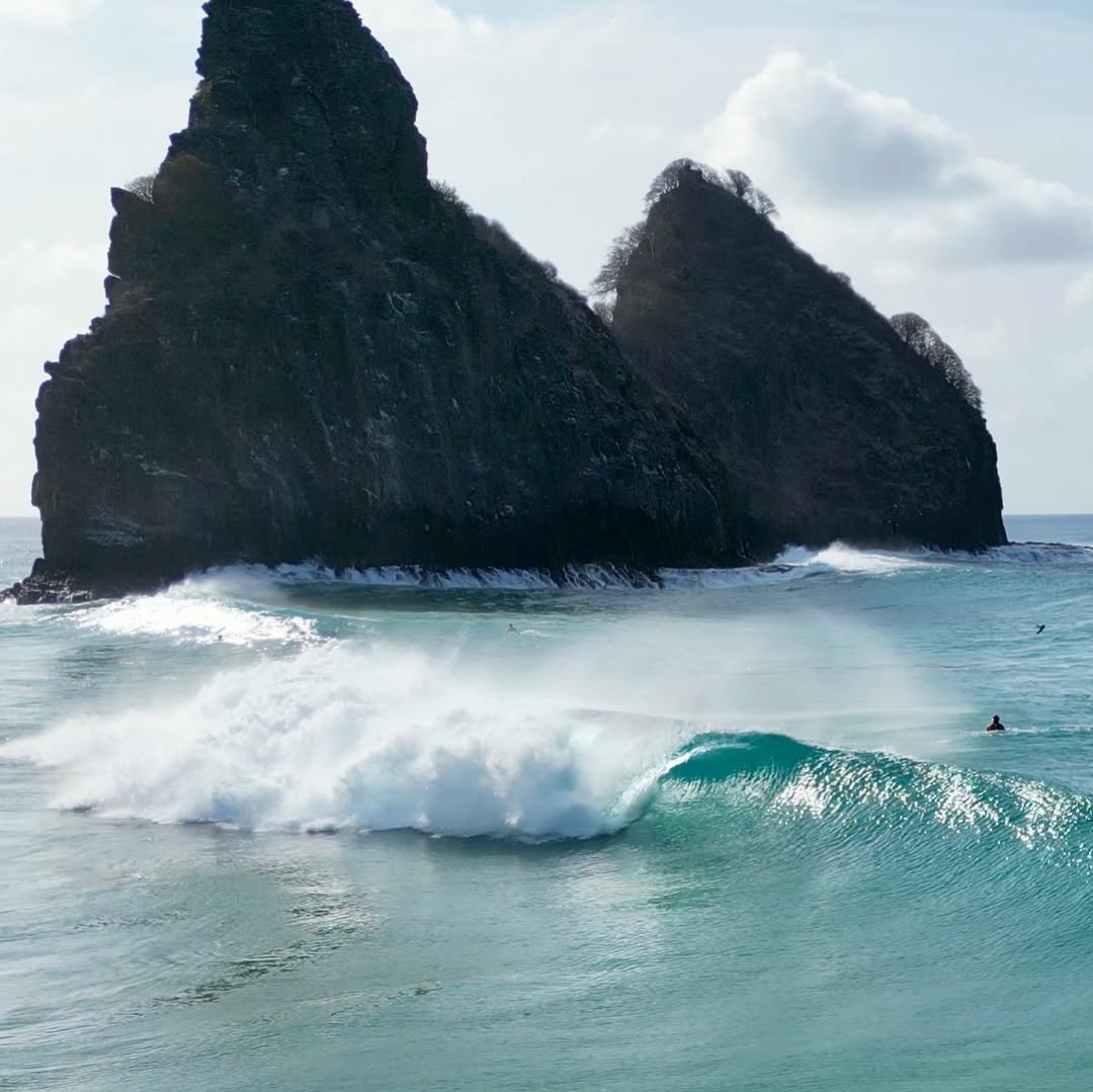 Photo shared by Surfguru Oficial on January 06, 2026 tagging @alanrangelfilmes. May be an image of surfboard, wetsuit, ocean, beach, Haystack Rock, water, coast and text.
