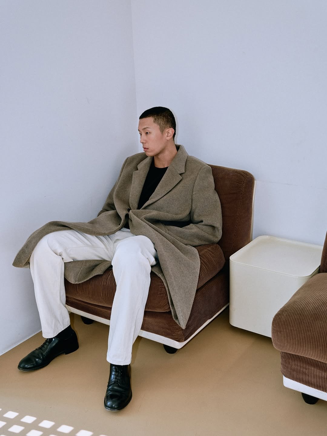 Photo by SYSTEM, SYSTEM HOMME on December 04, 2025. May be an image of one or more people, duffle coat, overcoat, suit, wingtip shoes, turtleneck, chaise lounge and text.