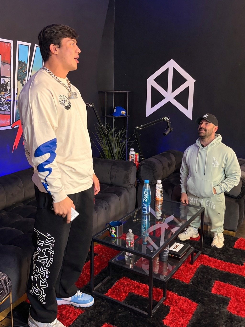 Photo by TOGI on January 06, 2026. May be an image of standing, television, sweatsuit, sweatpants, microphone, sweatshirt and text.