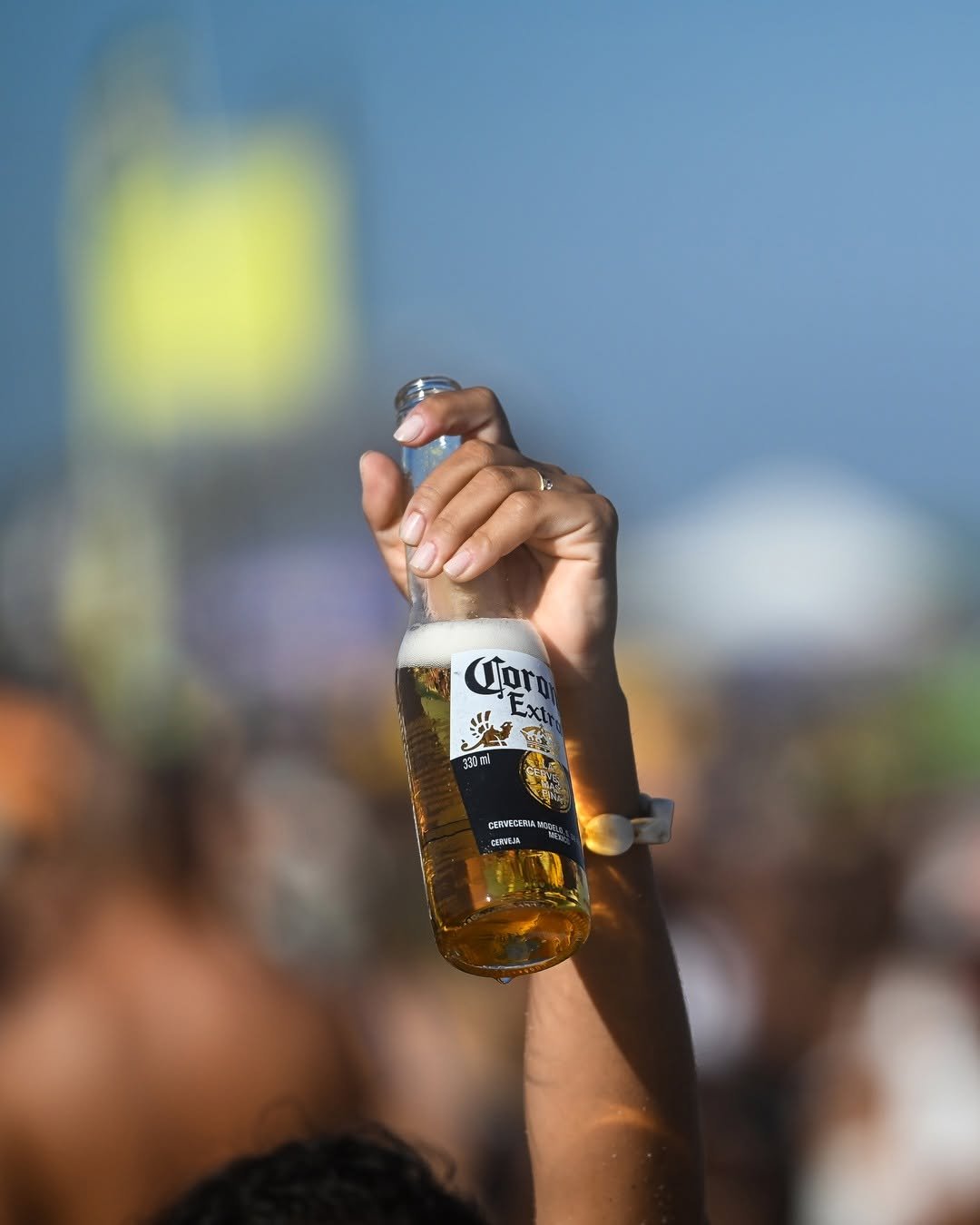 A hand holding a bottle of Corona Extra beer against a blurred background.