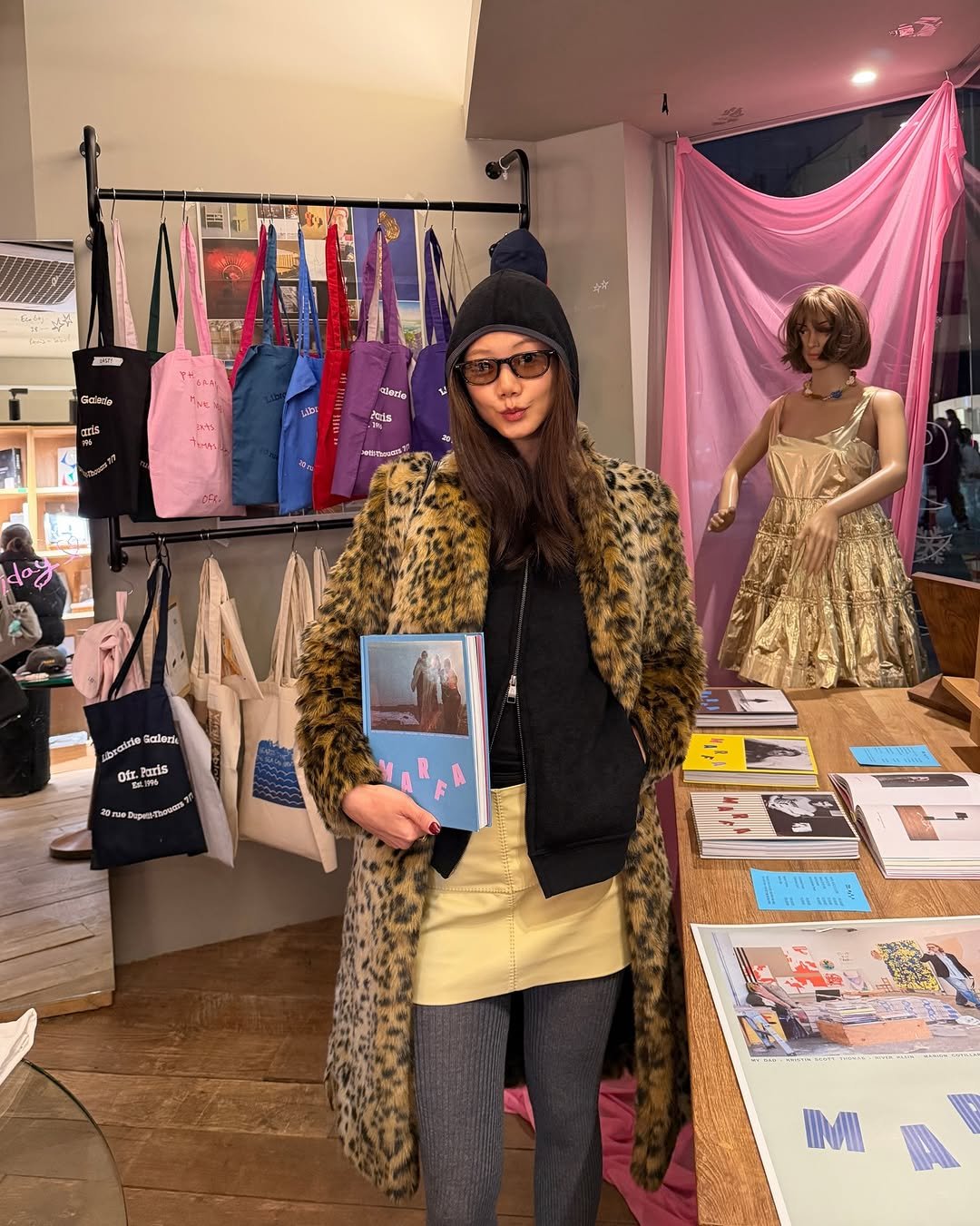 Photo shared by 예지 Yeji 🐿️ KIM on December 28, 2025 tagging @marfajournal, and @ofrseoul. May be an image of duffle coat, fur coat, parka, book, magazine, newsstand, hat shop and text.