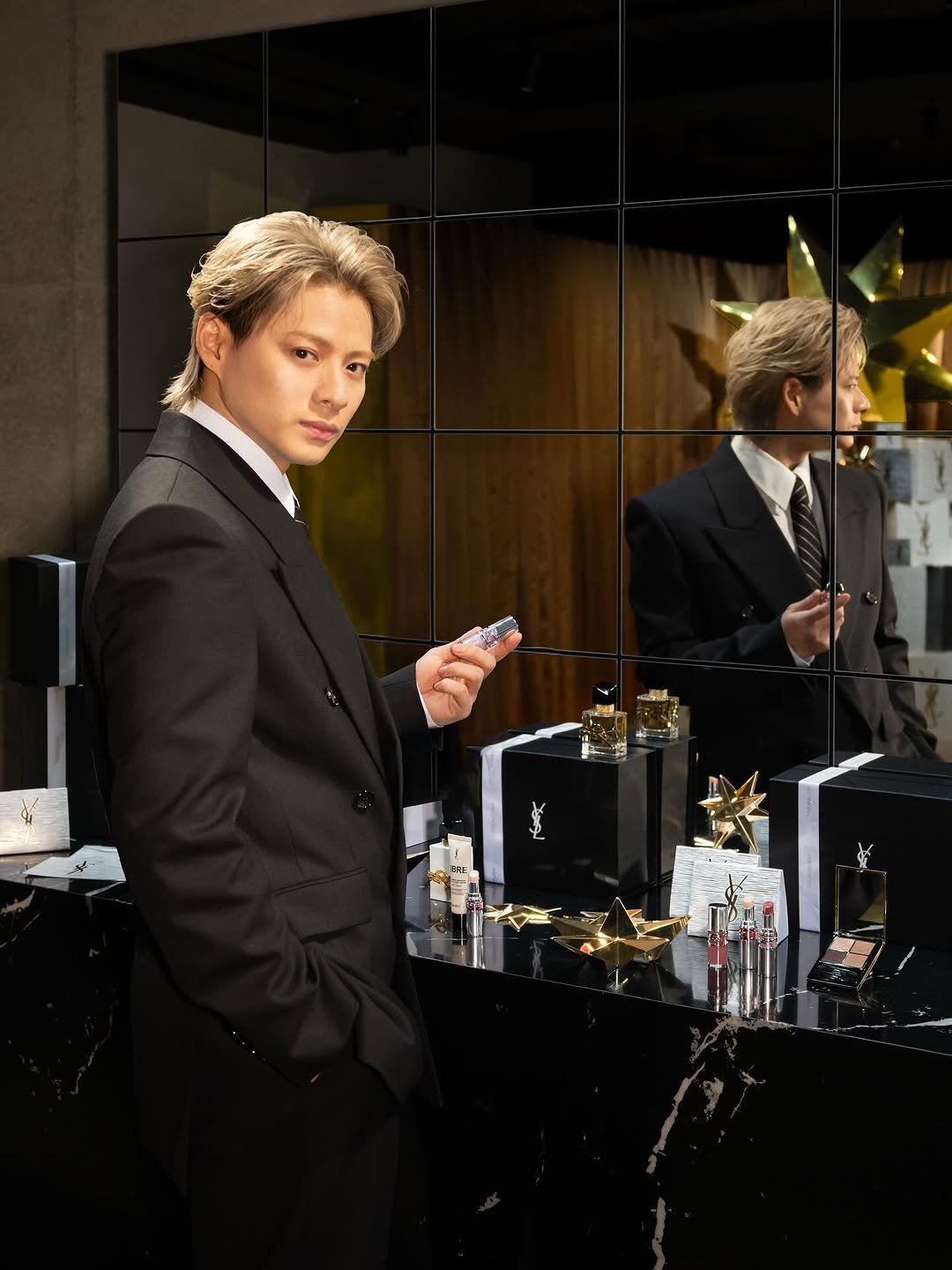 Photo shared by YSL Beauty Official on November 17, 2025 tagging @sho_h_desyo. May be an image of one or more people, makeup, fragrance, mirror, dinner jacket, perfume, display case, blazer, suit, bolo tie and text.